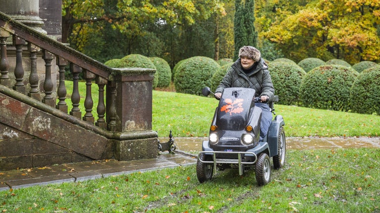 Visitor on a mobility Tramper with autumn leaves and stairs in the background.